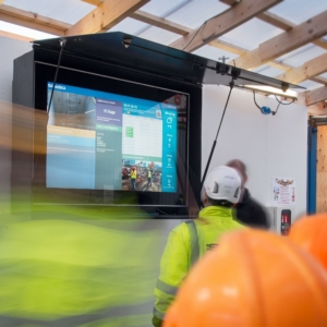 Workers and site management gathered for a morning meeting in front of the screen